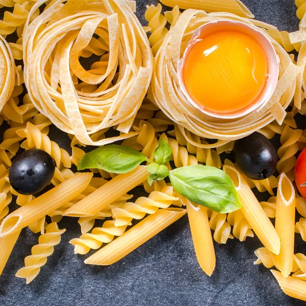 An assortment of fresh pasta shapes including fusilli and penne, topped with a raw egg yolk and fresh basil leaves.