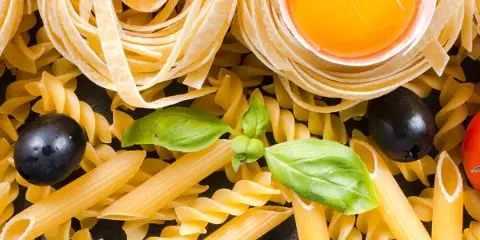 An assortment of fresh pasta shapes including fusilli and penne, topped with a raw egg yolk and fresh basil leaves.