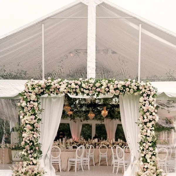 A wedding reception setup inside a white tent featuring a floral arch and round tables.
