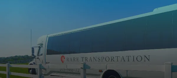 A white passenger bus with 'RARE TRANSPORTATION' branding parked outdoors.