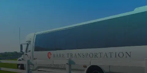 A white passenger bus with 'RARE TRANSPORTATION' branding parked outdoors.