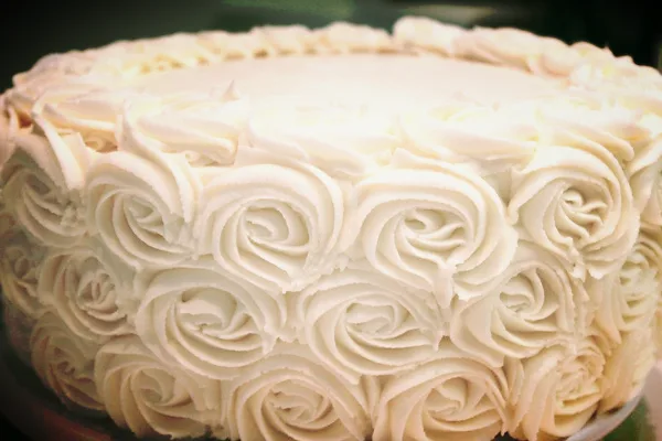 A close-up photograph of a white cake decorated with piped rosette frosting.