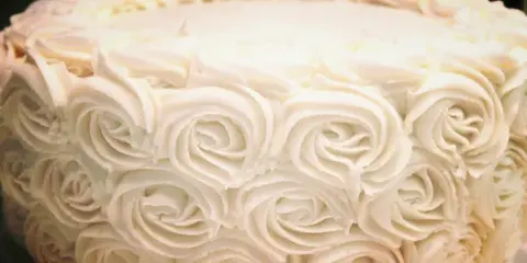 A close-up photograph of a white cake decorated with piped rosette frosting.