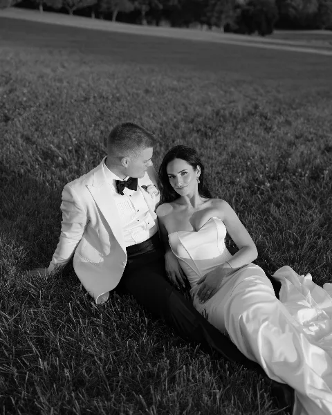 Black and white photograph of a bride and groom sitting together on a grassy lawn.