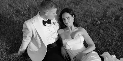 Black and white photograph of a bride and groom sitting together on a grassy lawn.