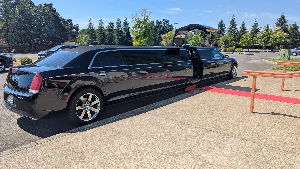 A black luxury limousine parked on a paved surface with its door open, revealing a red interior carpet.