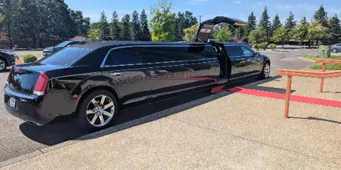 A black luxury limousine parked on a paved surface with its door open, revealing a red interior carpet.