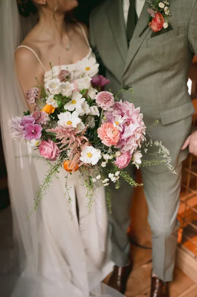 A bride and groom holding a large, colorful wedding bouquet featuring pink, white, and purple flowers.