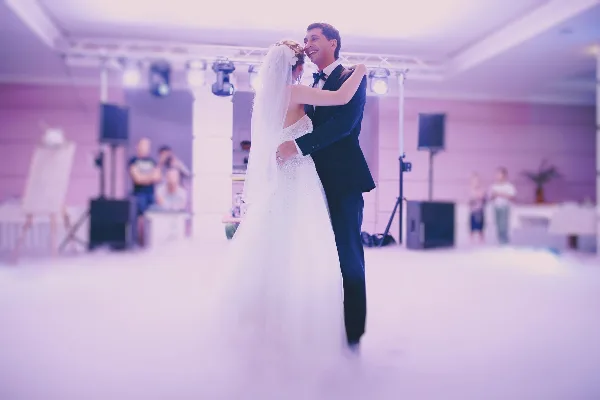 A bride and groom sharing a first dance at a wedding reception with professional stage lighting and sound equipment in the background.
