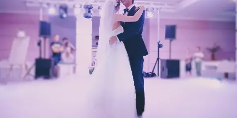 A bride and groom sharing a first dance at a wedding reception with professional stage lighting and sound equipment in the background.