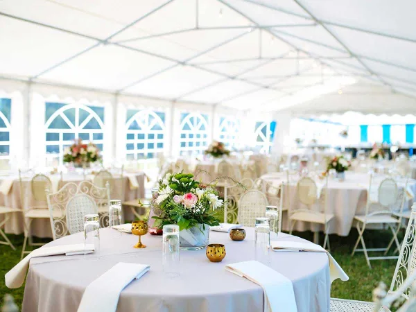 Interior view of a white event tent with round tables, white chairs, and floral centerpieces.