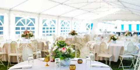 Interior view of a white event tent with round tables, white chairs, and floral centerpieces.