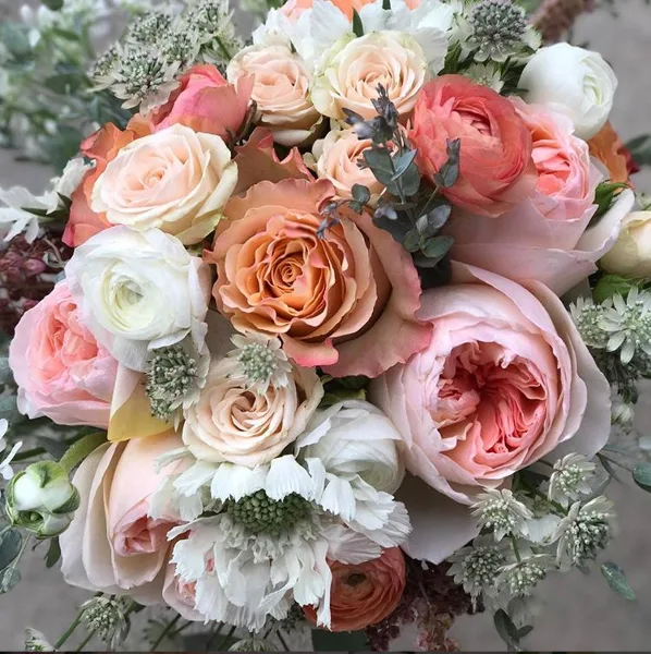 A close-up photograph of a fresh flower bouquet containing peach, pink, and white roses with greenery.