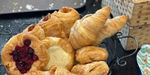 A wire basket filled with assorted baked pastries, including croissants and fruit-filled danishes, displayed in a bakery setting.