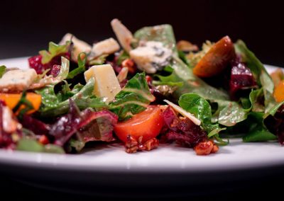 A close-up of a fresh salad with mixed greens, tomatoes, nuts, and cheese on a white plate.