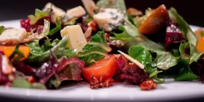 A close-up of a fresh salad with mixed greens, tomatoes, nuts, and cheese on a white plate.