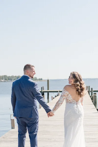 A bride and groom holding hands on a wooden pier by the water.
