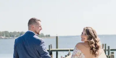 A bride and groom holding hands on a wooden pier by the water.