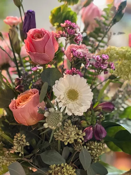 A close-up photograph of a fresh flower bouquet containing pink roses, a white daisy, and greenery.