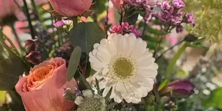 A close-up photograph of a fresh flower bouquet containing pink roses, a white daisy, and greenery.