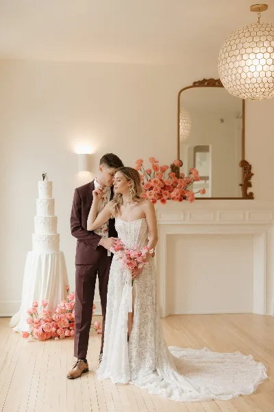 A bride and groom standing together in a bright, elegant room with a wedding cake and floral arrangements.