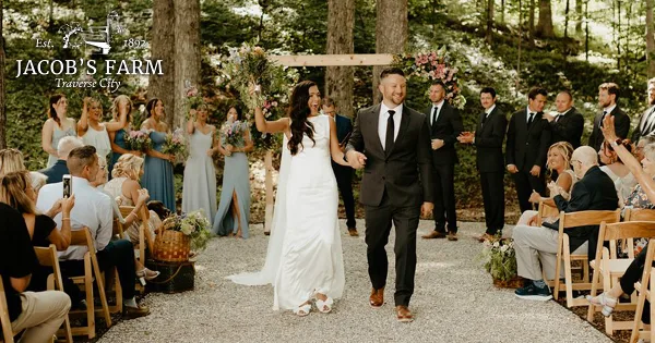 A bride and groom walking down a gravel aisle during an outdoor wedding ceremony at a farm venue.