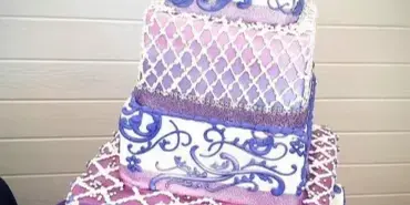 A five-tier square wedding cake decorated with purple and white patterns and a bride and groom topper.