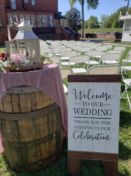 Outdoor wedding ceremony setup with rows of white chairs, a welcome sign, and floral decorations in front of a historic building.
