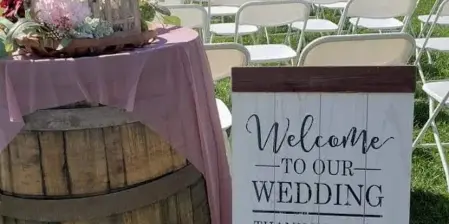 Outdoor wedding ceremony setup with rows of white chairs, a welcome sign, and floral decorations in front of a historic building.