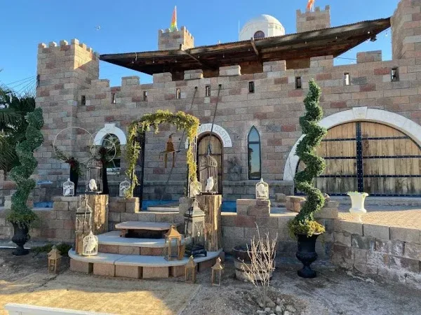 A stone castle facade featuring a decorated wedding arch, steps, and topiary plants.
