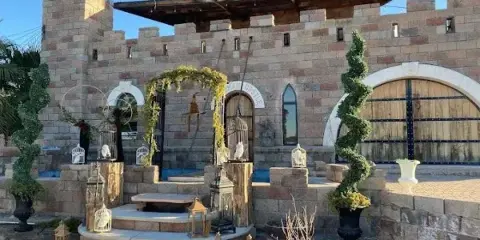 A stone castle facade featuring a decorated wedding arch, steps, and topiary plants.