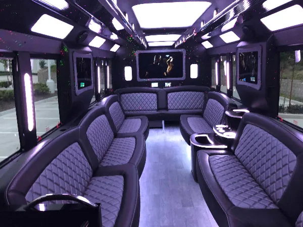 Interior view of a luxury party bus with black leather seating and ambient lighting.
