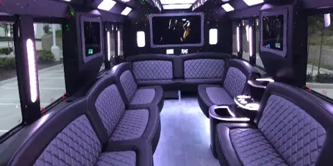 Interior view of a luxury party bus with black leather seating and ambient lighting.