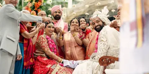 A bride and groom participate in a traditional Hindu wedding ceremony, holding a sacred thread together while surrounded by family members.