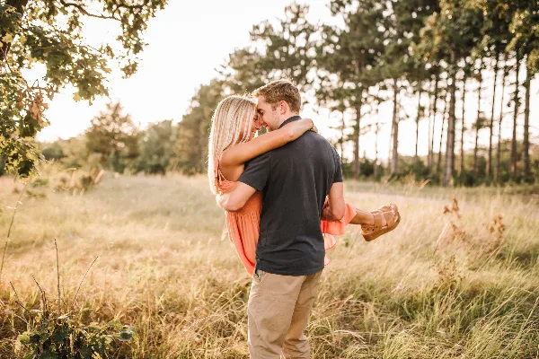 A couple embracing in a sunlit grassy field with trees in the background.