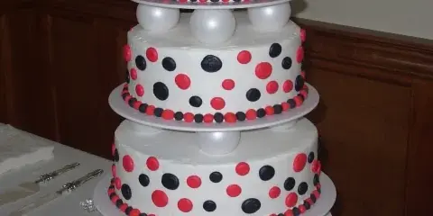 A four-tier white wedding cake decorated with red and black polka dots and topped with red roses.
