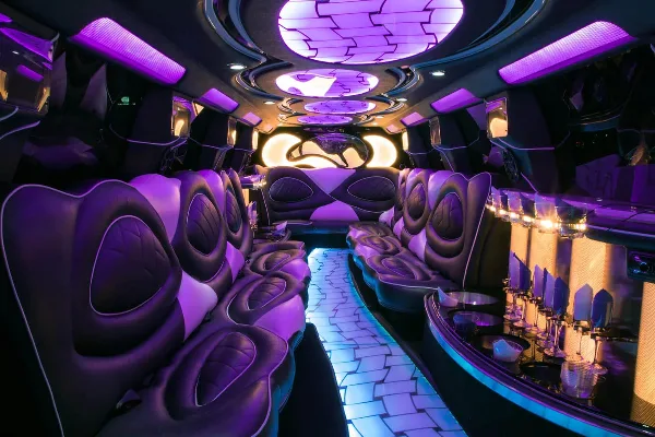 Interior of a luxury party bus with purple ambient lighting, plush seating, and a bar area.