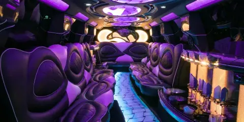 Interior of a luxury party bus with purple ambient lighting, plush seating, and a bar area.