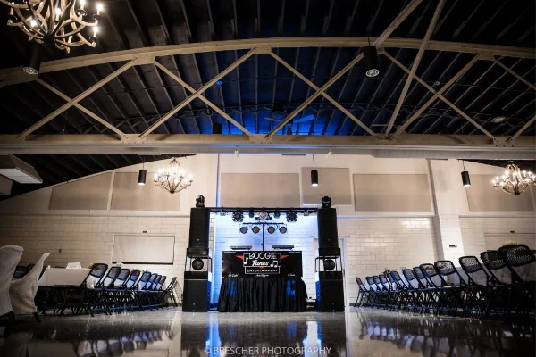 A professional DJ booth with branded table and speakers set up in a wedding reception hall.