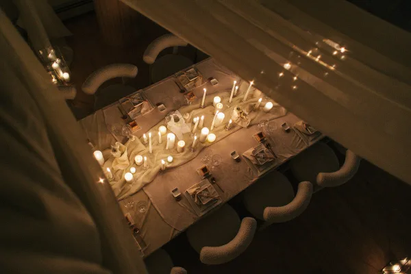 Overhead view of a candlelit event table with linens, place settings, and upholstered chairs.