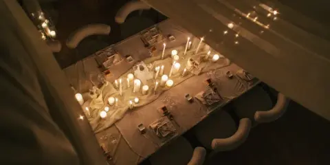 Overhead view of a candlelit event table with linens, place settings, and upholstered chairs.
