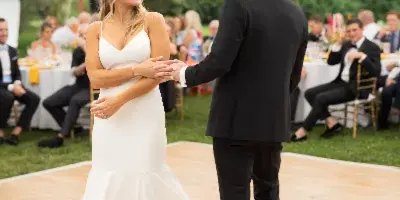 A bride and groom dancing on a wooden dance floor at an outdoor wedding reception under a white tent.
