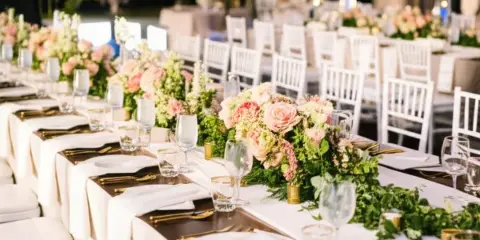Wedding reception tables set with white chiavari chairs, floral centerpieces, and glassware.