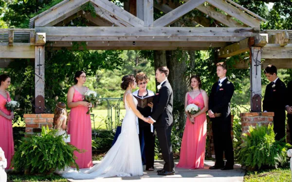 Ann McKenzie officiating a wedding ceremony outdoors with a bride and groom at an altar, surrounded by bridesmaids and groomsmen.