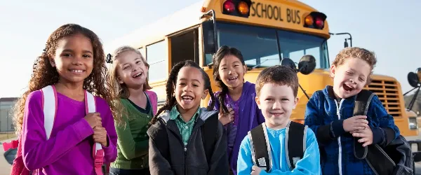 A group of smiling children standing in front of a yellow school bus.