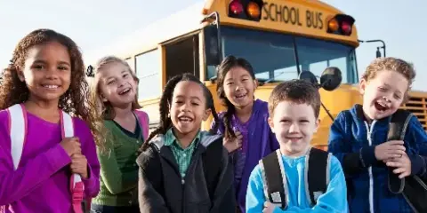 A group of smiling children standing in front of a yellow school bus.