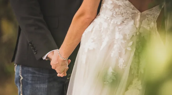 Close-up of a bride in a lace wedding dress and a groom in a dark suit holding hands.