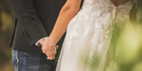 Close-up of a bride in a lace wedding dress and a groom in a dark suit holding hands.