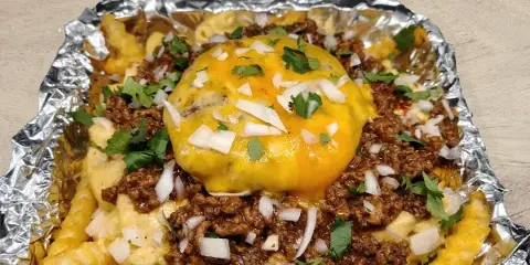 A catering plate featuring crispy fries, mac and cheese, meat sauce, and a cheeseburger served in a foil-lined container.