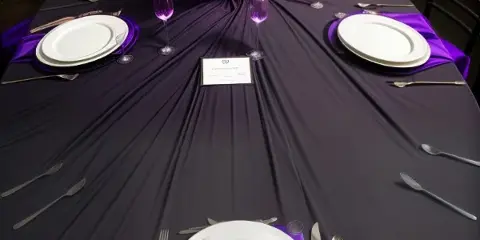 Round banquet table dressed in deep purple linen with chiavari chairs, plated settings and floral centerpiece by Party Pizazz